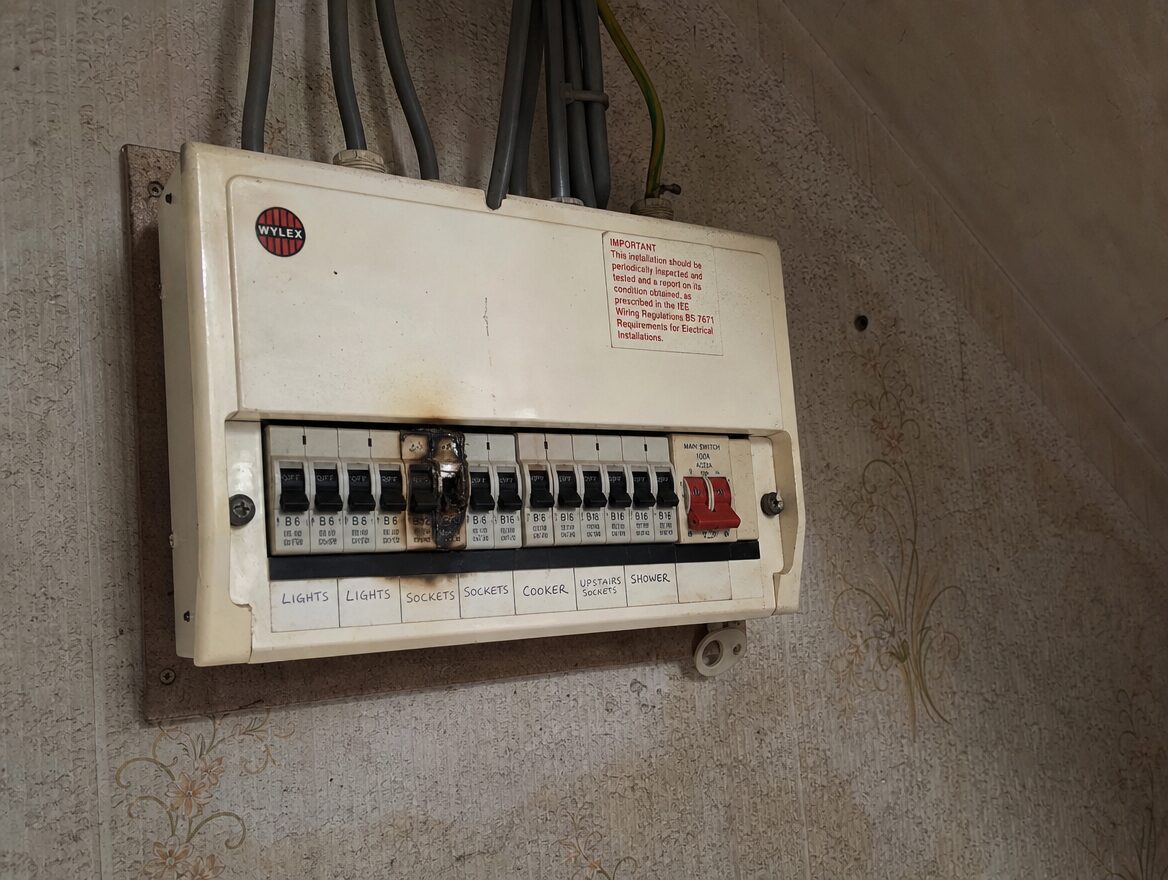 Old fuse box with scorch marks in a rented house hallway